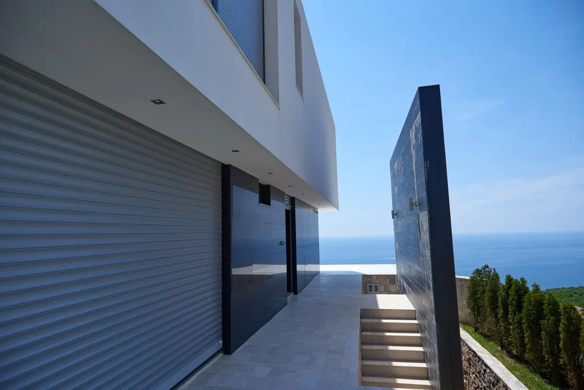 Villa contemporaine dont la grande baie est fermée par un volet roulant à lames aluminium, mer en arrière-plan